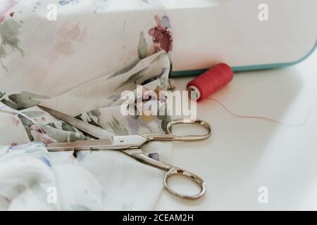Closeup thin cotton thread lying on table near sharp scissors and piece of ornamental cloth in dressmaker workshop Stock Photo