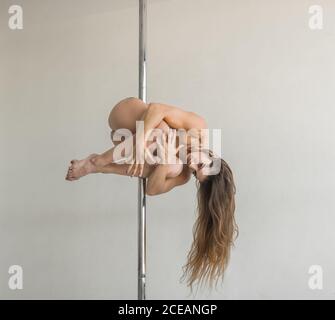 Young slim strong Woman practicing on pole in light room studio Stock Photo