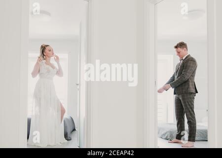 Beautiful young Woman in white dress and handsome guy in elegant suit preparing for wedding ceremony in different hotel rooms Stock Photo