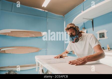 man in respirator measuring surf board in workshop Stock Photo