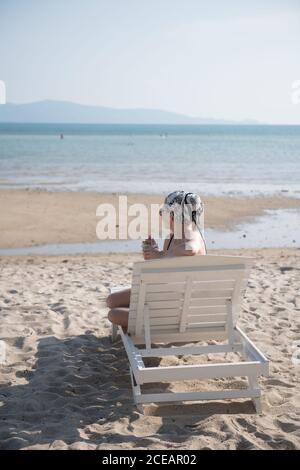 Young Woman sitting and looking away on deck chair on beach in Thailand. Stock Photo