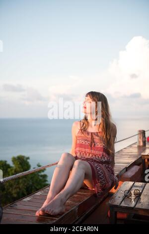 Side view of unrecognizable Woman sitting on boardwalk and looking away at the ocean in Thailand. Stock Photo