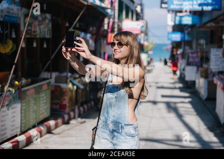 Cheerful young Woman taking selfie with camera while standing on street in Thailand. Stock Photo