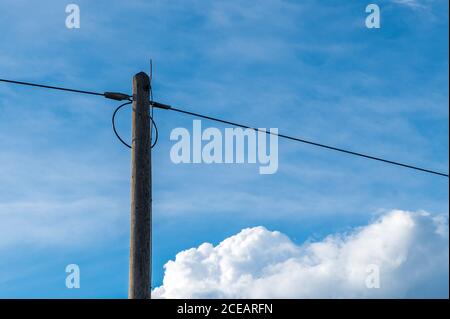 A telephone pole in front of a blue sky with clouds Stock Photo