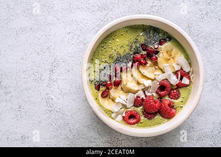 From above view of bowl with green smoothie garnished with various seeds and berries with banana. Stock Photo