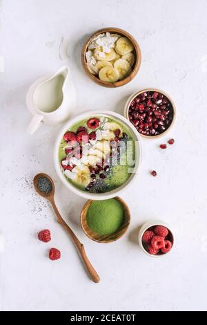 Flat lay of bowl with healthy smoothie for breakfast in composition with various additives as fruit and matcha powder. Stock Photo