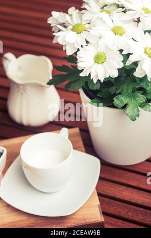 Small cup and jug of fresh milk standing on wooden table near ceramic pot with beautiful flowers Stock Photo