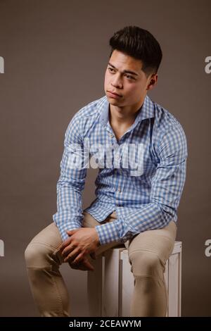 Young male in shirt and trousers sitting with serious expression Stock Photo