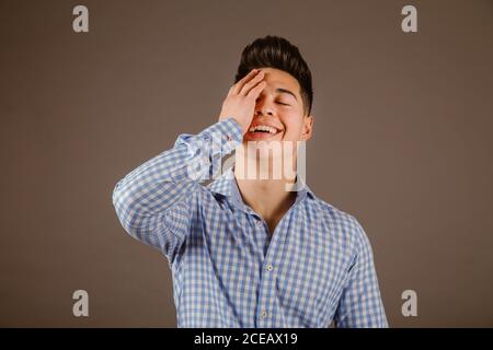 Handsome man covering eyes with hand and smiling on gray background Stock Photo