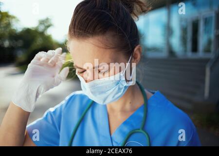 covid-19 pandemic. stressed modern physician woman in uniform with stethoscope and medical mask outside near clinic. Stock Photo