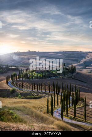 Sunset over beautiful S curved road in Tuscany, Italy - woman in red dress walking into distance Stock Photo