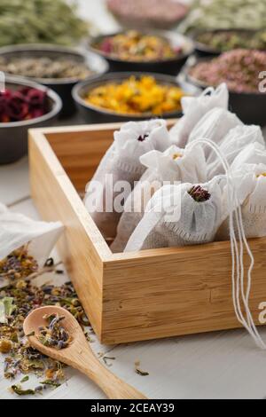 Wooden box of filter tea bags filled with dry medicinal herbs and flowers. Black bowls of medicinal plants on background. Alternative medicine. Stock Photo