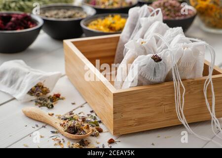 Wooden box of tea bags filled with dry medicinal herbs. Black bowls of medicinal plants on background. Alternative medicine Stock Photo