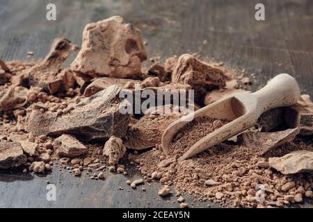 Pieces of grated cocoa. Natural chocolate lumps and wooden scoop on dark wooden table. Stock Photo