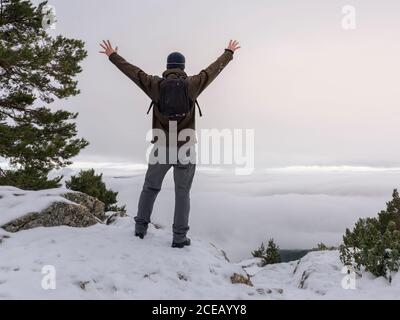 Hiker and his dog looking in the snowy mountains at foggy sky background. Stock Photo