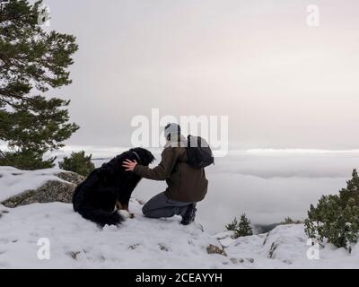 Hiker and his dog looking in the snowy mountains at foggy sky background. Stock Photo