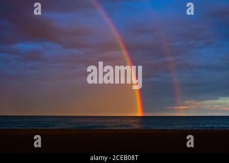 Beautiful rainbow appearing on cloudy sky over calm sea. Stock Photo