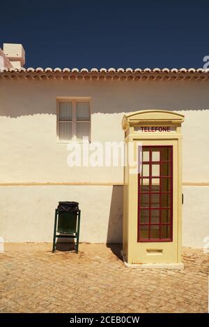 Vintage call-box with red wooden windows standing with green iron trash can at white building on blue sky background Stock Photo