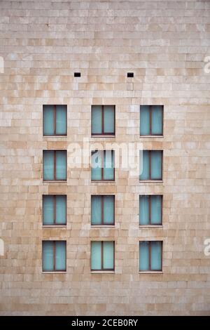 Light brown brick wall of building with little similar closed windows in Bilbao Stock Photo