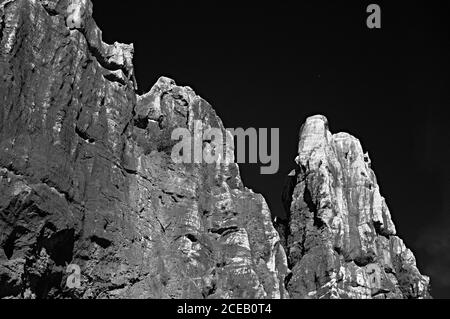 High steep sharp rocks with trees growing at bottom on background of sky in black and white colors Stock Photo