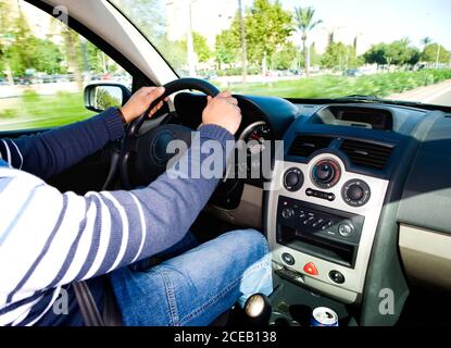 Crop shot of man holding hands on steering wheel and driving car on background of green park on street Stock Photo