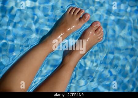 Crop from above view of legs of person lying on clear transparent water in swimming pool Stock Photo