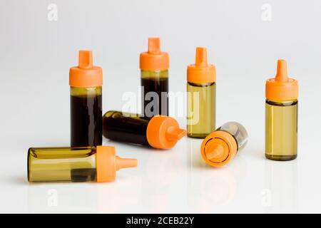 Plastic tubes with orange caps filled with dark and light liquids lying on shiny surface isolated on white background Stock Photo