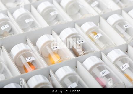 From above view of many plastic vessels with numbers and colorful pills lying in white paper box in soft focus Stock Photo
