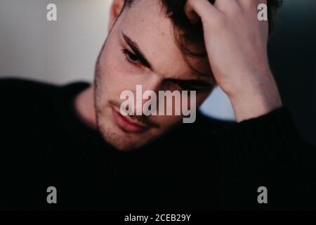 Closeup young thoughtful guy in black sweater with hand on hairs looking downstairs in Madrid, Spain Stock Photo