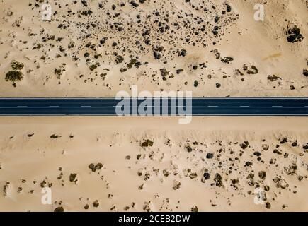 Drone view from above of straight line of paved road in dry sandy land of desert, Spain Stock Photo
