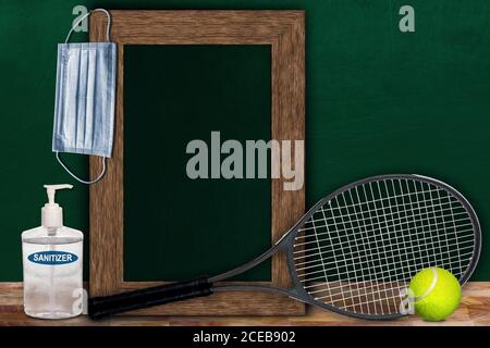 COVID-19 new normal sports concept in a classroom setting showing framed chalkboard with copy space and tennis racket and ball on wooden table. Stock Photo