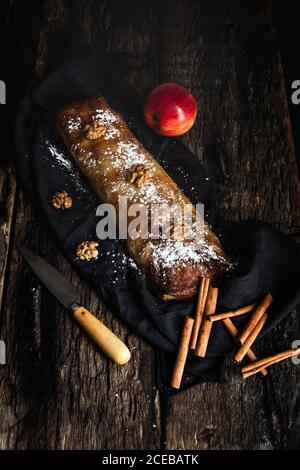 Homemade apple strudel with nuts, raisins and cinnamon. On dark wood background Stock Photo