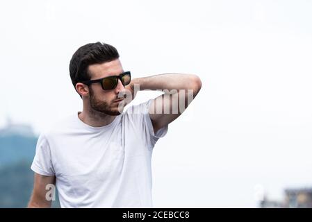 Thoughtful young man in sunglasses and white t-shirt standing and looking away Stock Photo