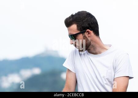 Thoughtful young man in sunglasses and white t-shirt standing and looking away Stock Photo