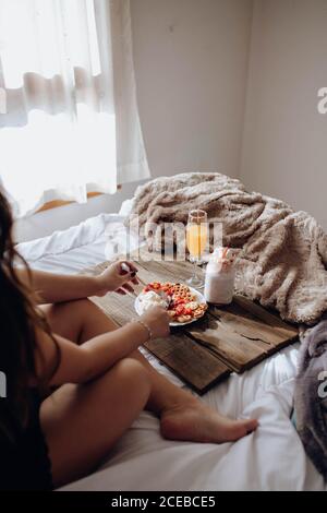 Young Woman eating appetizing waffles and tasty drinks on tray on bed Stock Photo