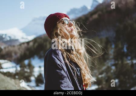 Side view of Woman in warm clothes and sunglasses enjoying the sun in winter mountains. Stock Photo