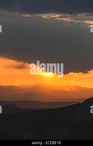 Beautiful golden sun rays of sunset sky covered with dark clouds above mountains silhouette Stock Photo