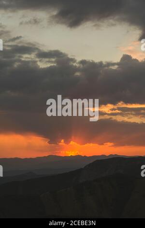 Beautiful golden sun rays of sunset sky covered with dark clouds above mountains silhouette Stock Photo