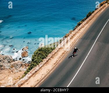 From above skateboarder man riding on asphalt road on the hill in sunny day. Stock Photo