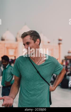 Happy young guy in green t-shirt looking away on street on blurred background Stock Photo