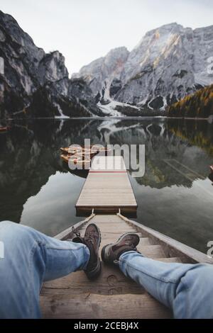 Legs of anonymous man lying on steps near pier and calm surface of Pragser Wildsee in Dolomites, Italy Stock Photo