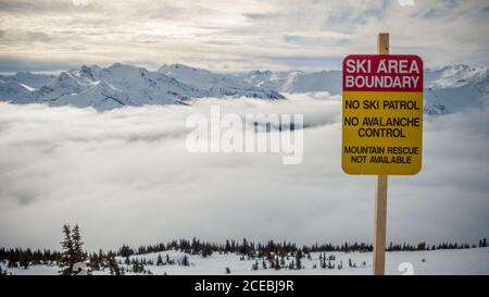 Picturesque view of peak of mountains in clouds and warning sign with ski area boundary words in Canada Stock Photo