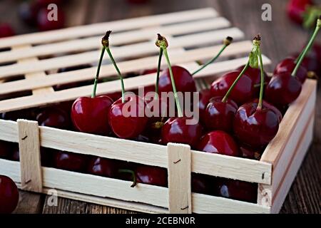 Close-up shot of small wooden box filled with shiny bright red cherry on table Stock Photo
