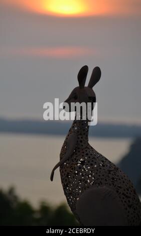 Silhouette of a metal kangaroo sculpture overlooking the inlet estuary in the coastal town of Mallacoota with a fiery orange sky with clouds Stock Photo