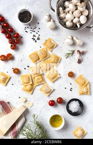 From above uncooked ravioli and different spices with tomatoes and mushrooms on a table Stock Photo