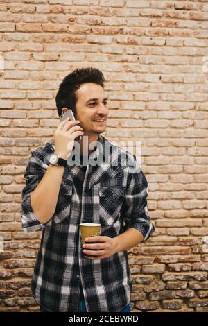 Young man with cup talking on smartphone Stock Photo