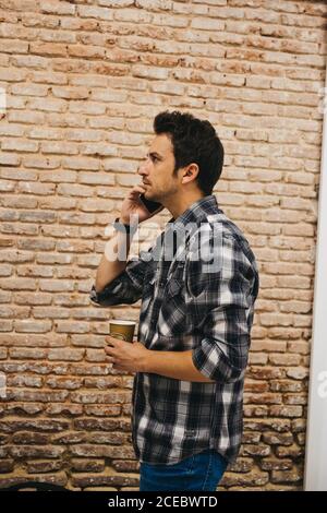 Young man with cup talking on smartphone Stock Photo