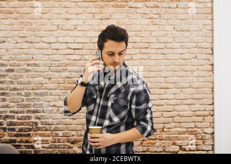 Young man with cup talking on smartphone Stock Photo