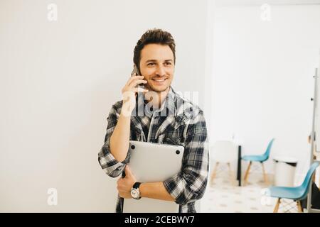 Young man with laptop talking on smartphone Stock Photo