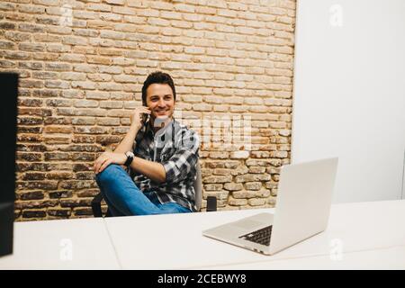 Young man using smartphone at table with laptop Stock Photo